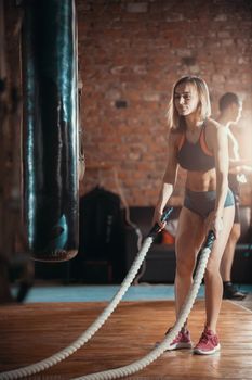 An athletic woman doing crossfit in the gym. Holding the ropes in the hands. Mid shot