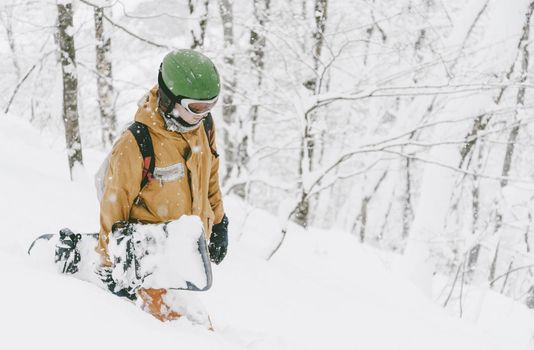 Freerider young man walking with snowboard in winter forest among snow