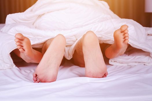 couple feet seen from under blanket on a bed