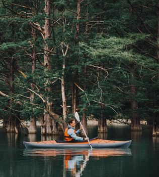 Young man kayaking on lake on background of trees in summer.