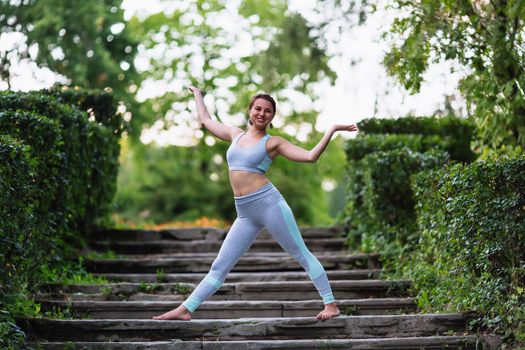 Pretty woman doing yoga exercises in the park on the stairs