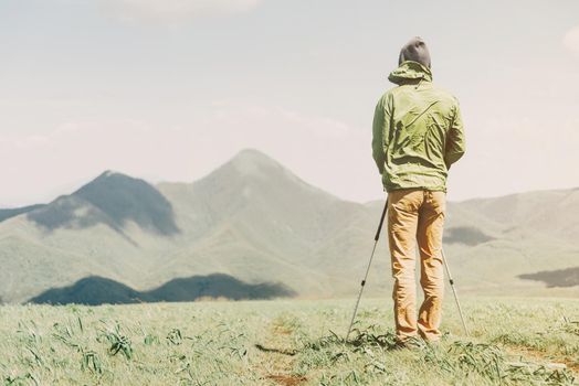 Explorer young man with trekking poles walking in summer mountains, rear view.