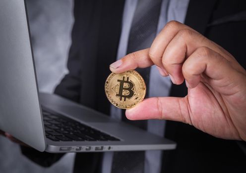 hand holding golden bitcoin with a laptop computer 