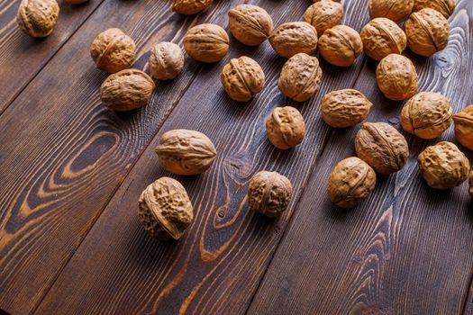 many walnuts with shells randomly scattered on brown wooden table surface, close-up perspective view with selective focus