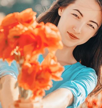 Outdoor portrait of smiling beautiful young woman giving a bouquet of poppies flowers, looking at camera.