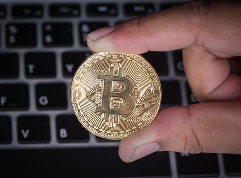 hand holding golden bitcoin with a laptop computer background