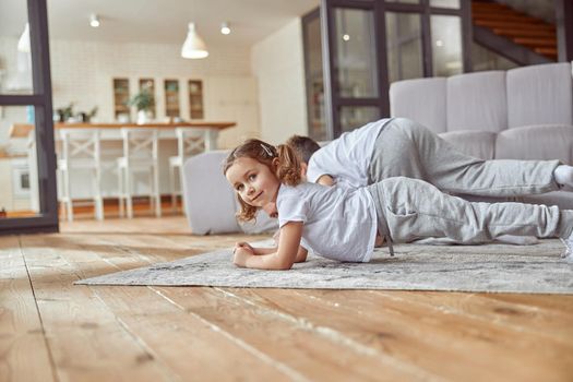 Low angle waist up portrait of smiling daughter doing plank position with older brother and father in living room