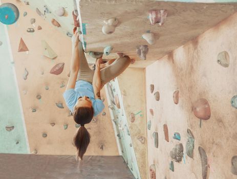Climber young woman training on practical wall indoor, bouldering.