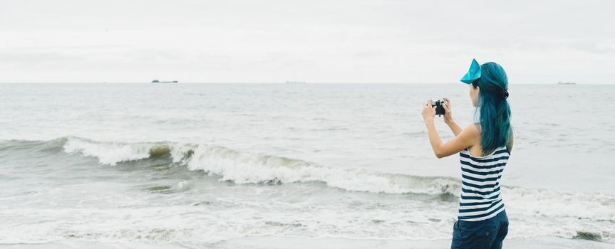 Tourist young woman in sailor style taking photographs of sea in summer.