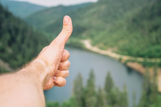 Traveler young man showing gesture thumb up on background of summer landscape, point of view shot.