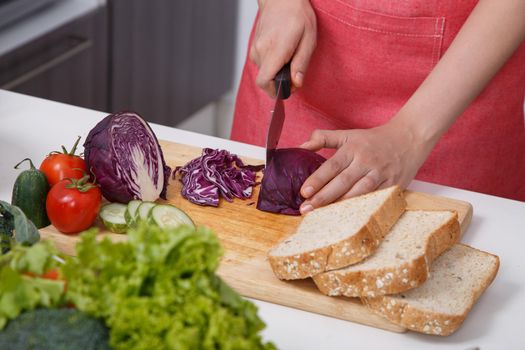 hand cutting purple cabbage on board in kitchen room at home