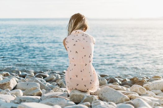 Young woman sitting on pebble beach and enjoying view of calm sea.