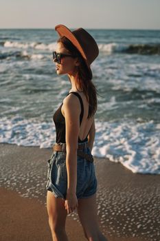 cheerful woman in sunglasses and a hat walks along the ocean. High quality photo