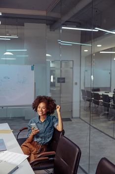 Smiling multiethnic lady working in the office while holding smartphone. Business, employment concept