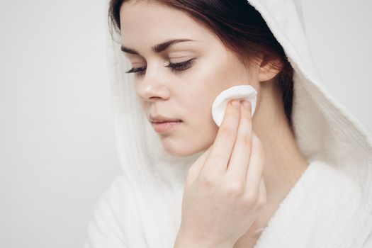 woman with a hood on her head wipes her face with a cotton pad skin care. High quality photo