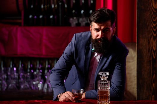 Barman luxury beverage concept. Man with beard holds glass with alcohol in bar. Waiter bartender in vintage vest with whiskey or scotch on tray