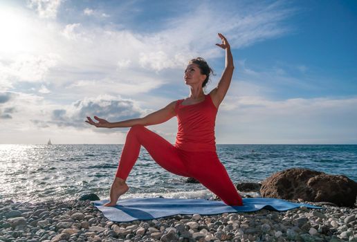 The woman in a red suit practicing yoga on stone at sunrise near the sea. Young beautiful girl in a red bathing suit sits on the seashore in lotus position. Yoga. Healthy lifestyle. Meditation