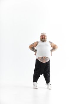 Happy fat man with big belly and tattoes in sports wear posing on white background