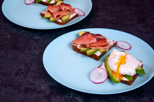 Bread Toasts with Cream Cheese, Avocado, Poached Egg and Salmon Fish on Dark Background. Healthy Breakfast or Appetizer Concept.