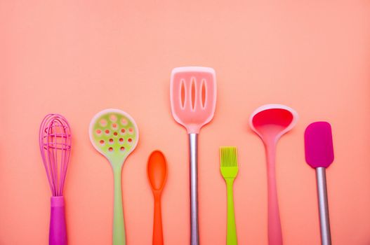 Various Colored Silicone Kitchen Utensils on Coral Background. Copy Space For Your Text.