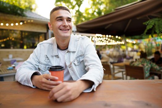 Young man with cup of coffee sitting in outdoor cafe, close up