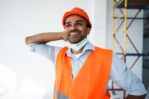 Portrait of mixed race man builder in workwear and hardhat wearing medical mask, close up photo