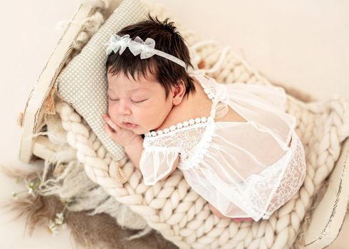 Nice newborn in lace dress sleeping on small bed