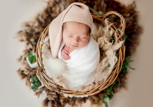 Cute newborn in hat with big balabon sleeping in basket
