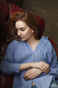 young woman in blue striped shirt. portrait of thoughtful model. caucasian skinny female with long brown hair lies on couch at home. natural pretty lady lying on sofa