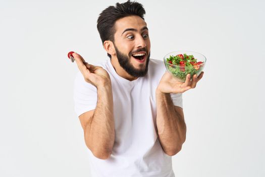 Cheerful man in a white T-shirt with a plate of light green and a healthy meal. High quality photo
