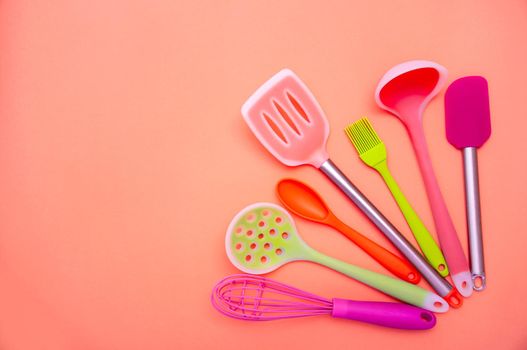 Various Colored Silicone Kitchen Utensils on Coral Background. Copy Space For Your Text.