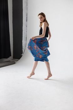 pretty woman in blue skirt with bare feet spinning around on white background. dancing movements of young lady, indoors portrait. caucasian skinny female with long brown hair dances on cyclorama