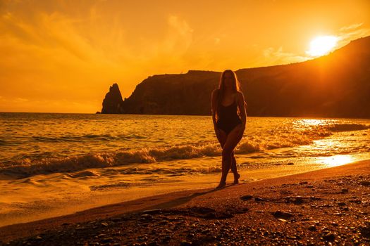 Selective focus. Happy carefree sensual woman with long hair in black swimwear posing at sunset beach. Silhouette of young beautiful playful positive woman outdoor. Summer vacation and trip concept.