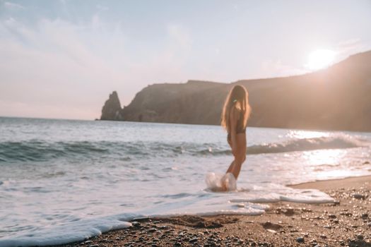 Selective focus. Happy carefree sensual woman with long hair in black swimwear posing at sunset beach. Silhouette of young beautiful playful positive woman outdoor. Summer vacation and trip concept.