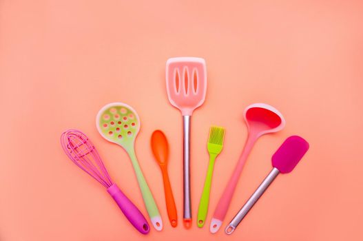 Various Colored Silicone Kitchen Utensils on Coral Background. Copy Space For Your Text.