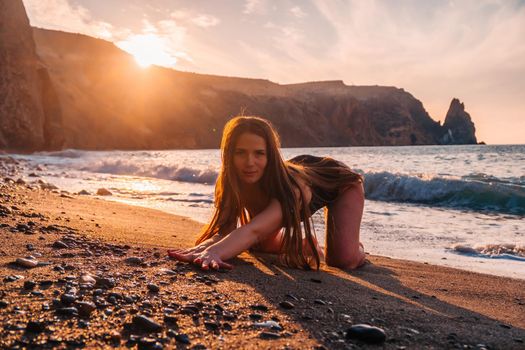 Selective focus. Happy carefree sensual woman with long hair in black swimwear posing at sunset beach. Silhouette of young beautiful playful positive woman outdoor. Summer vacation and trip concept.