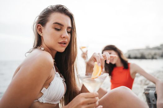 Two young female friends having a picnic on a beach drinking cocktails