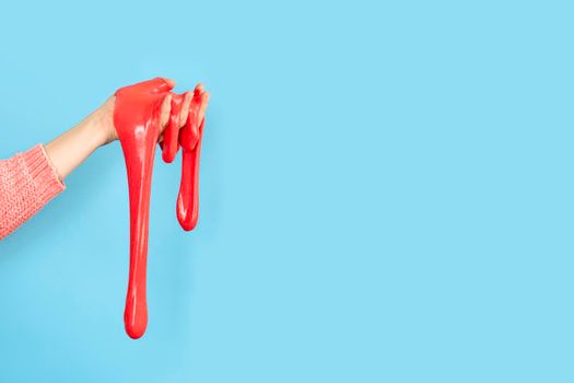 Close up on shiny Red or coral slime in the hand isolated on blue background. Fun and stress relief concept. Banner with copy space.