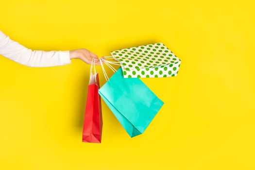 Shopping or sale concept. Female hand light holds colorful shopping paper bags isolated on yellow background. Sale banner