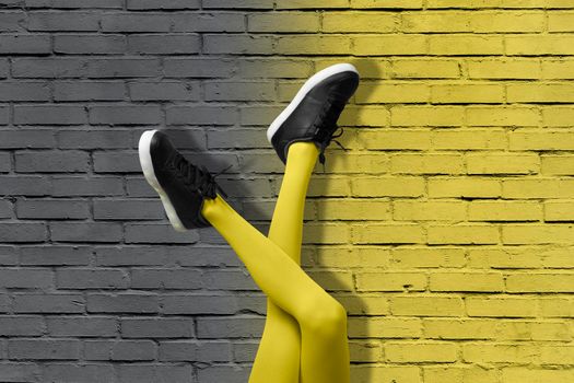 New Black female sneakers on long slender girl legs in yellow tights on background of gradient yellow and gray brick wall. Color of 2021 year pop art concept.