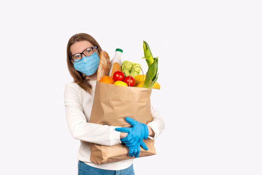 Safe food delivery or donation concept. Food delivery or shopping during coronavirus quarantine. Young woman in disposable gloves and face mask holding Box with food ingredients