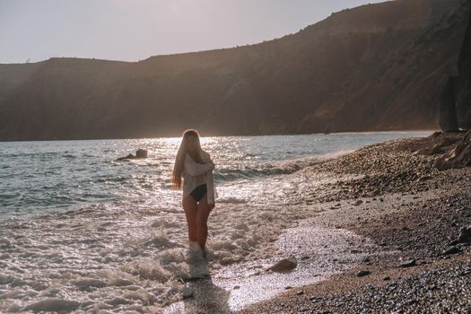 Selective focus. Happy carefree sensual woman with long hair in black swimwear posing at sunset beach. Silhouette of young beautiful playful positive woman outdoor. Summer vacation and trip concept.