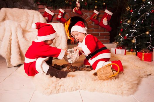 Children are sitting near fireplace and play with cones - Christmas decorations
