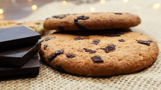 American chocolate chip cookies on a brown wooden table and on a linen napkin close-up. Traditional rounded crunchy dough with chocolate chips. Bakery. Delicious dessert, pastries. Rural still life