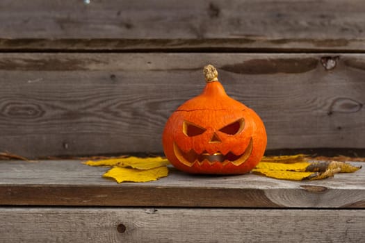 halloween scary pumpkin with eyes and mouth and yellow leaves on wooden background. Autumn Carved funny handmade Pumpkin