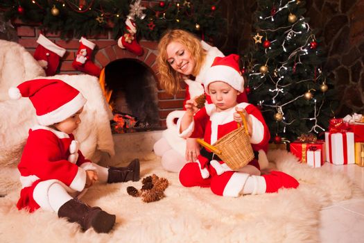 Mother with children are sitting near fireplace and play with cones - Christmas decorations