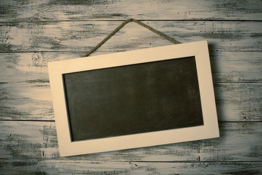 Empty chalkboard on the rope attached to shabby white wooden background