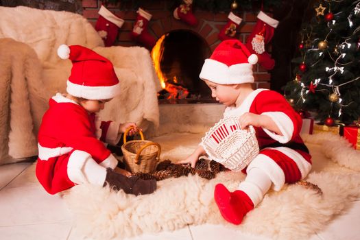 Children are sitting near fireplace and play with cones - Christmas decorations