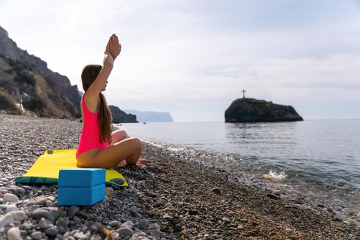 The woman in a red suit practicing yoga on stone at sunrise near the sea. Young beautiful girl in a red bathing suit sits on the seashore in lotus position. Yoga. Healthy lifestyle. Meditation