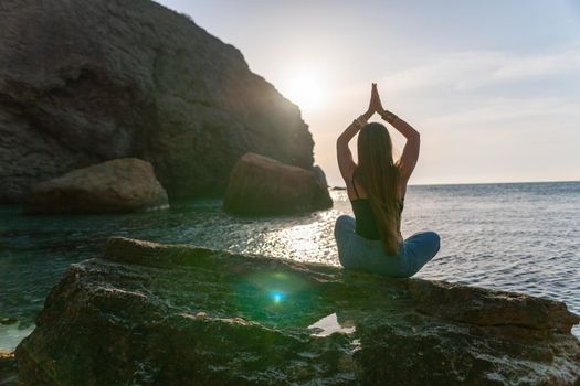 Young woman in swimsuit with long hair practicing stretching outdoors on yoga mat by the sea on a sunny day. Women's yoga fitness pilates routine. Healthy lifestyle, harmony and meditation concept.